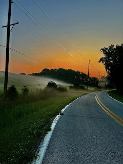 Country road curving through fogy hills at sunrise with colorful sky and power lines