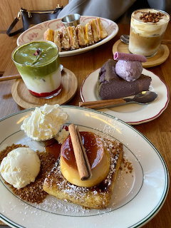 Overhead cafe table with assorted desserts: waffles, layered drinks, chocolate mousse, and pastries with ice cream
