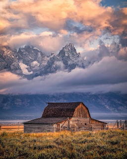 Wooden barn in meadow with snow-covered mountain peaks and colorful sunset sky