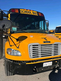 Front view of a yellow school bus parked outdoors under a blue sky