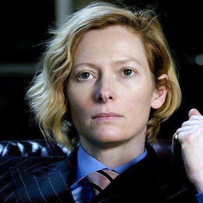 Blonde woman with short wavy hair in a dark pinstripe suit and striped tie
