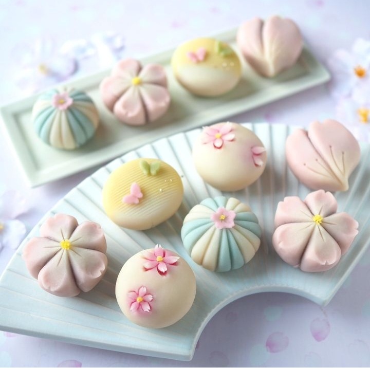 Pastel flower-shaped pastries on decorative trays in pink, blue, and cream colors