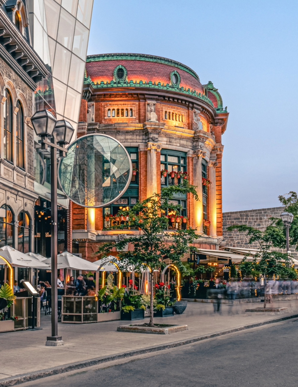 Illuminated Le Capitole historic building in Quebec City at dusk with ornate rounded facade and patios