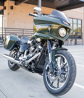Custom green Harley-Davidson touring motorcycle with chrome engine and custom wheel parked outside a building