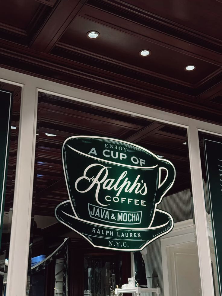 Glowing neon sign reading 'A Cup of Ralph's Coffee Java & Mocha Ralph Lauren N.Y.C.' in a shop window