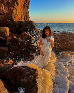 Woman in white dress on beach rocks at sunset with ocean waves