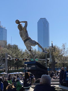 Statue of Dirk Nowitzki above a crowd with Dallas skyline behind it