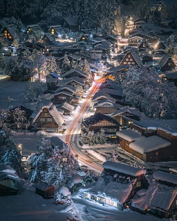 Snowy Shirakawa-go village at night with glowing houses and winding road light trails