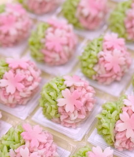 Rows of round green and pink pastries topped with pink cherry blossom decorations on clear trays