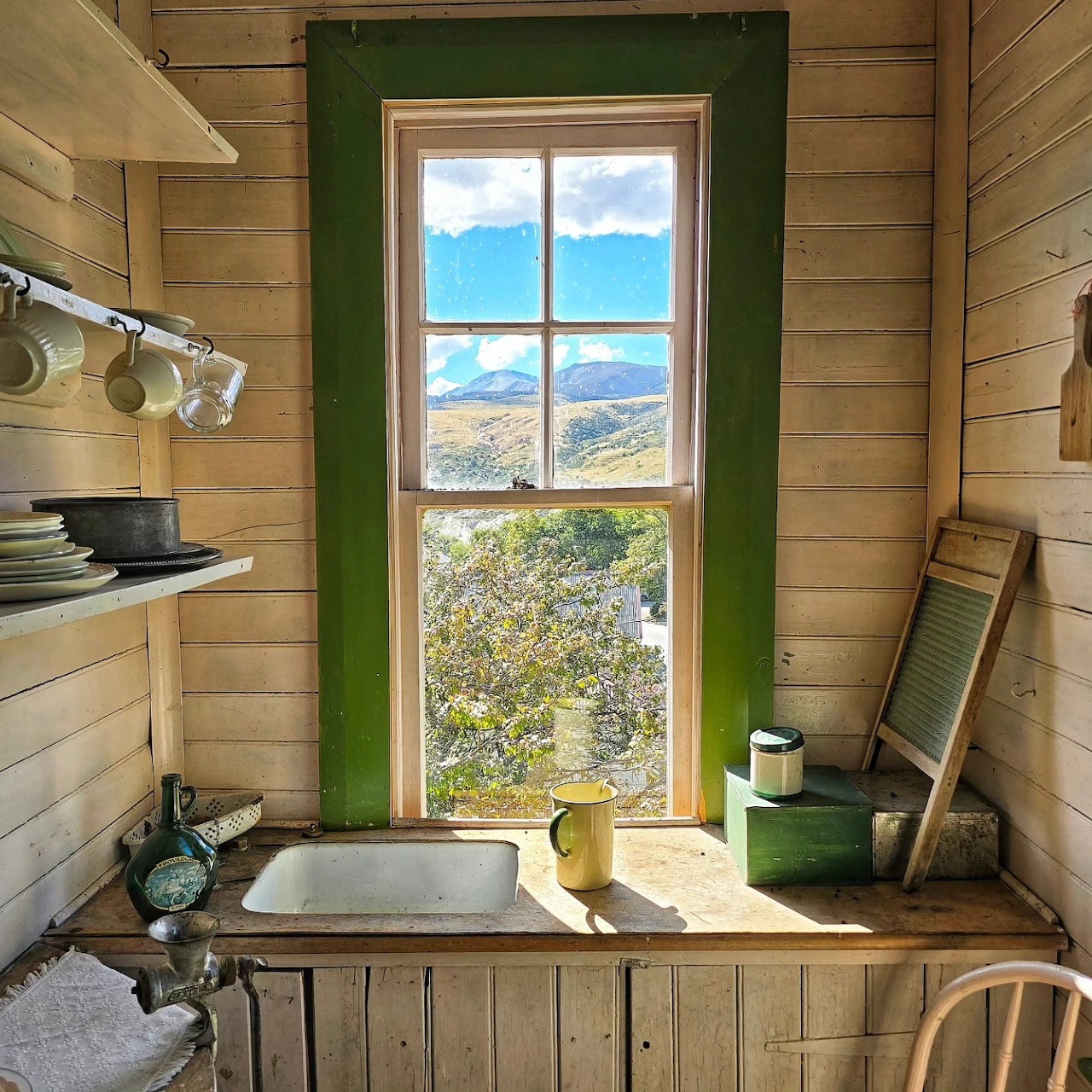 Rustic cabin kitchen with green window frame showing mountain lake view, wooden walls, and sink counter