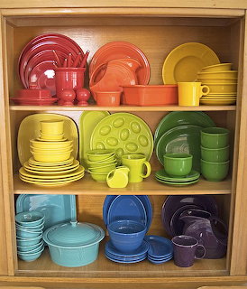 Wooden shelf displaying colorful Fiesta-style dishes arranged in rainbow order from red to purple