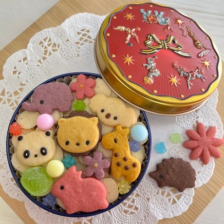 Assorted animal-shaped cookies in a tin with a red decorative lid on a doily