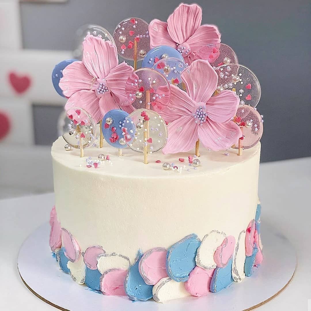White cake with pink flower toppers and colorful candy decorations