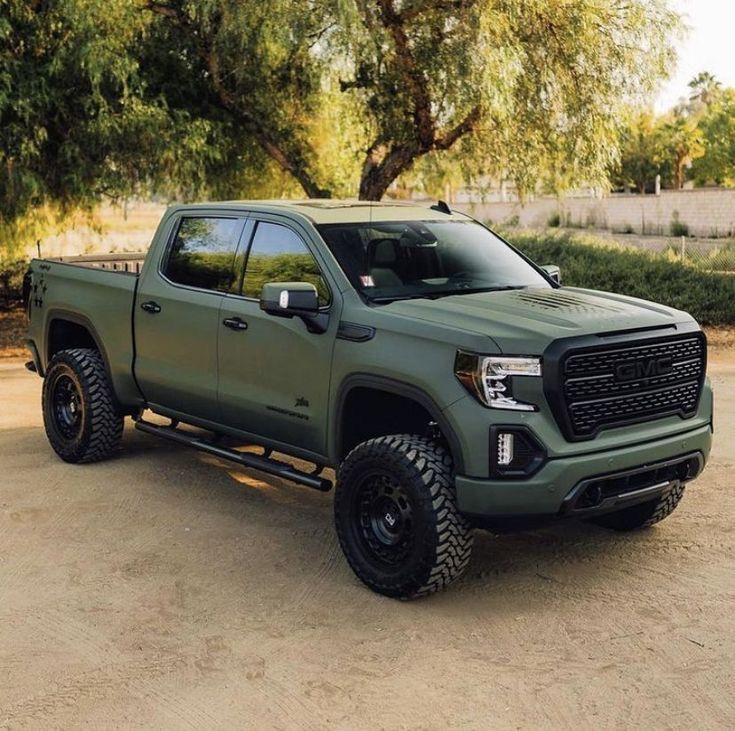 Matte green pickup truck parked on a dirt driveway under trees