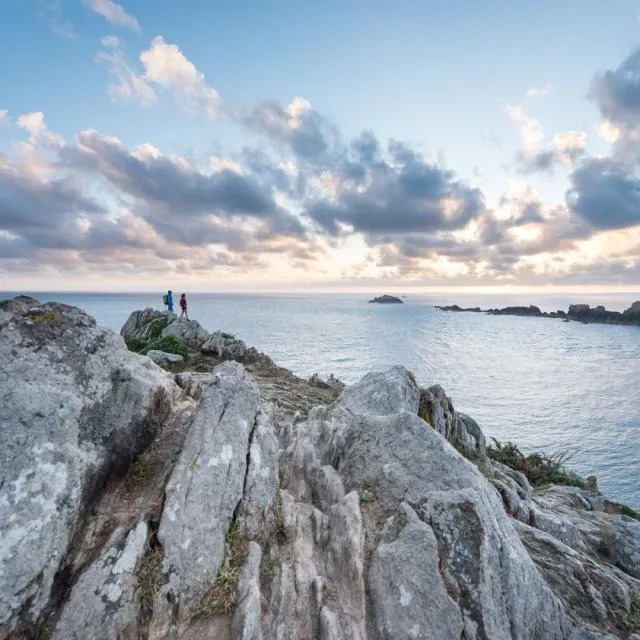 Rocky cliff at Pointe de Grouin overlooking the sea at sunrise with two distant figures on the rocks
