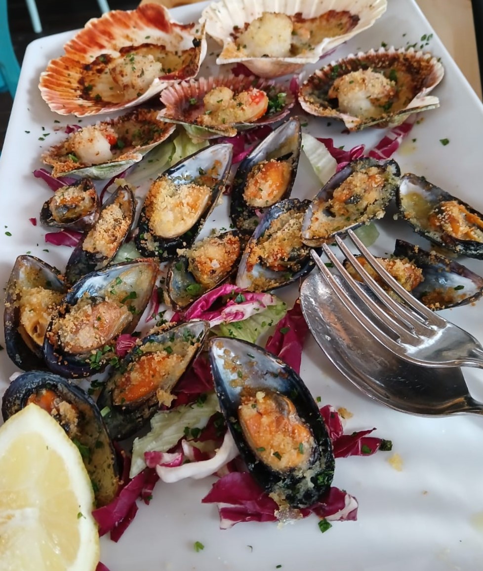 Platter of baked mussels and scallops with breadcrumb topping, lemon wedge, and garnish