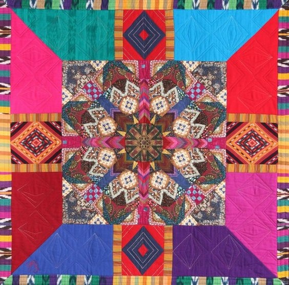Colorful quilted textile with central star pattern and geometric blocks in bright pink, turquoise, red and blue fabrics