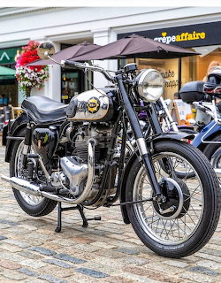 Black BSA classic motorcycle with chrome details and flower decoration on kickstand, displayed on brick pavement