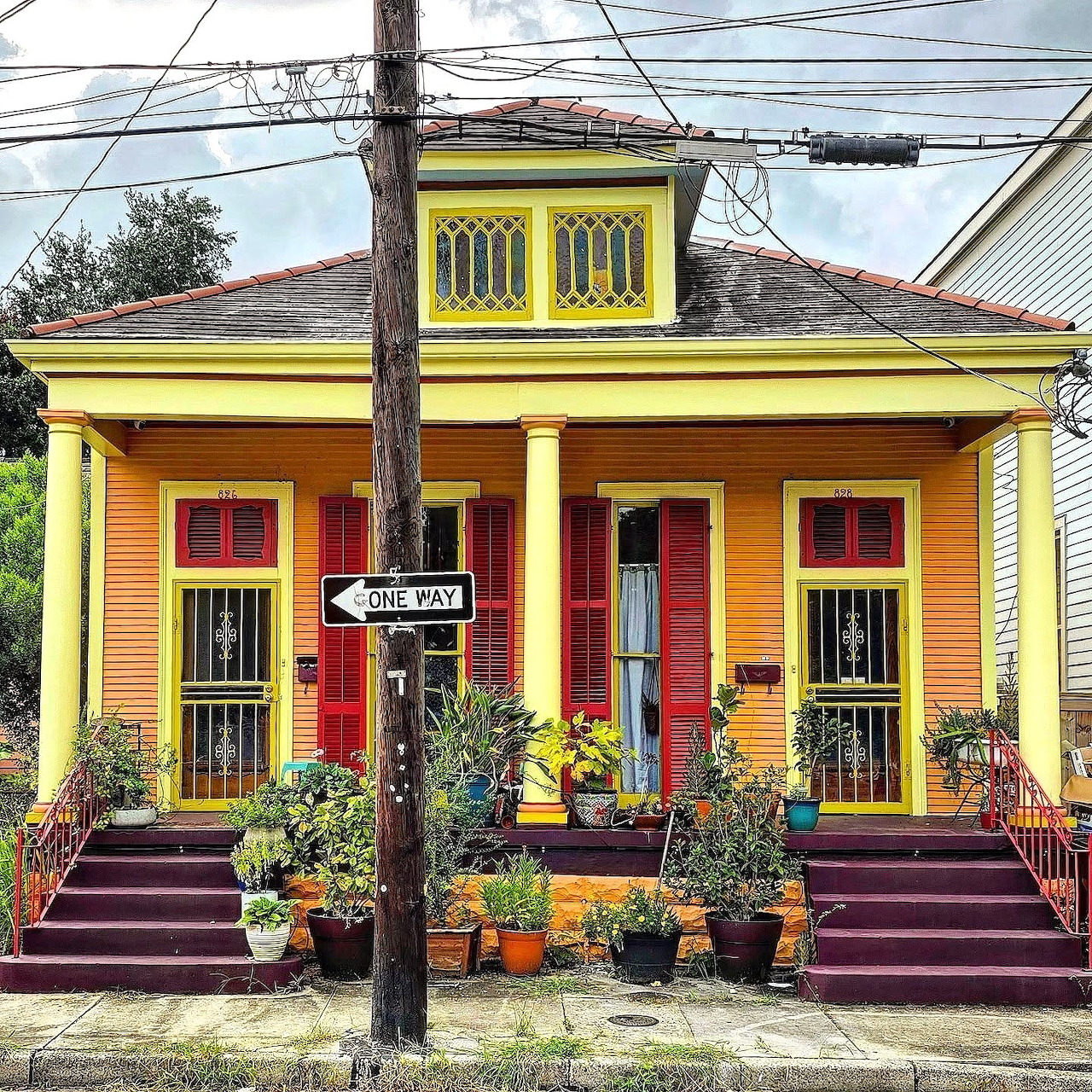 Yellow house with dual red doors, purple front steps, and planters on sidewalk under overcast sky