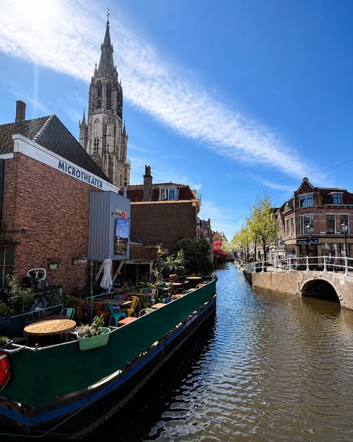 Canal in Delft lined with traditional Dutch houses and a bridge over still water.