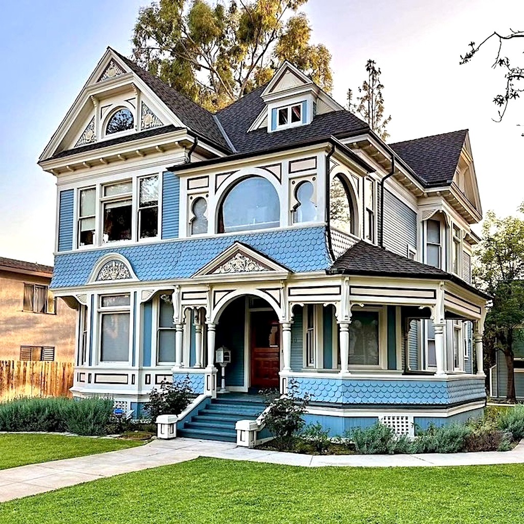 Blue Victorian house with white decorative trim, turret, and front porch surrounded by green lawn and trees