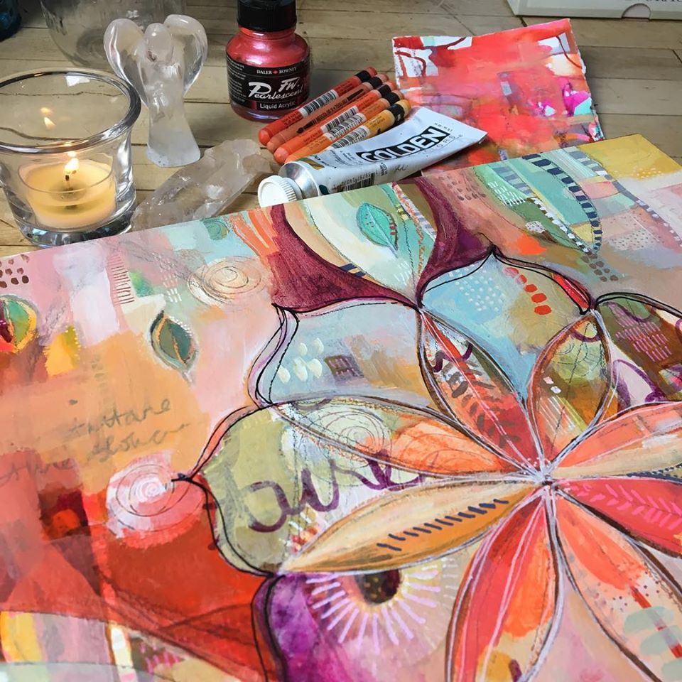 Colorful abstract collage painting with art supplies, pastel sticks, paint tubes, and a candle on a table