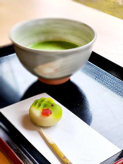 Japanese wagashi confection with matcha tea in ceramic bowl on black serving tray