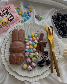 Chocolate Easter bunny on a white plate with candy eggs, blackberries, and gold fork and knife