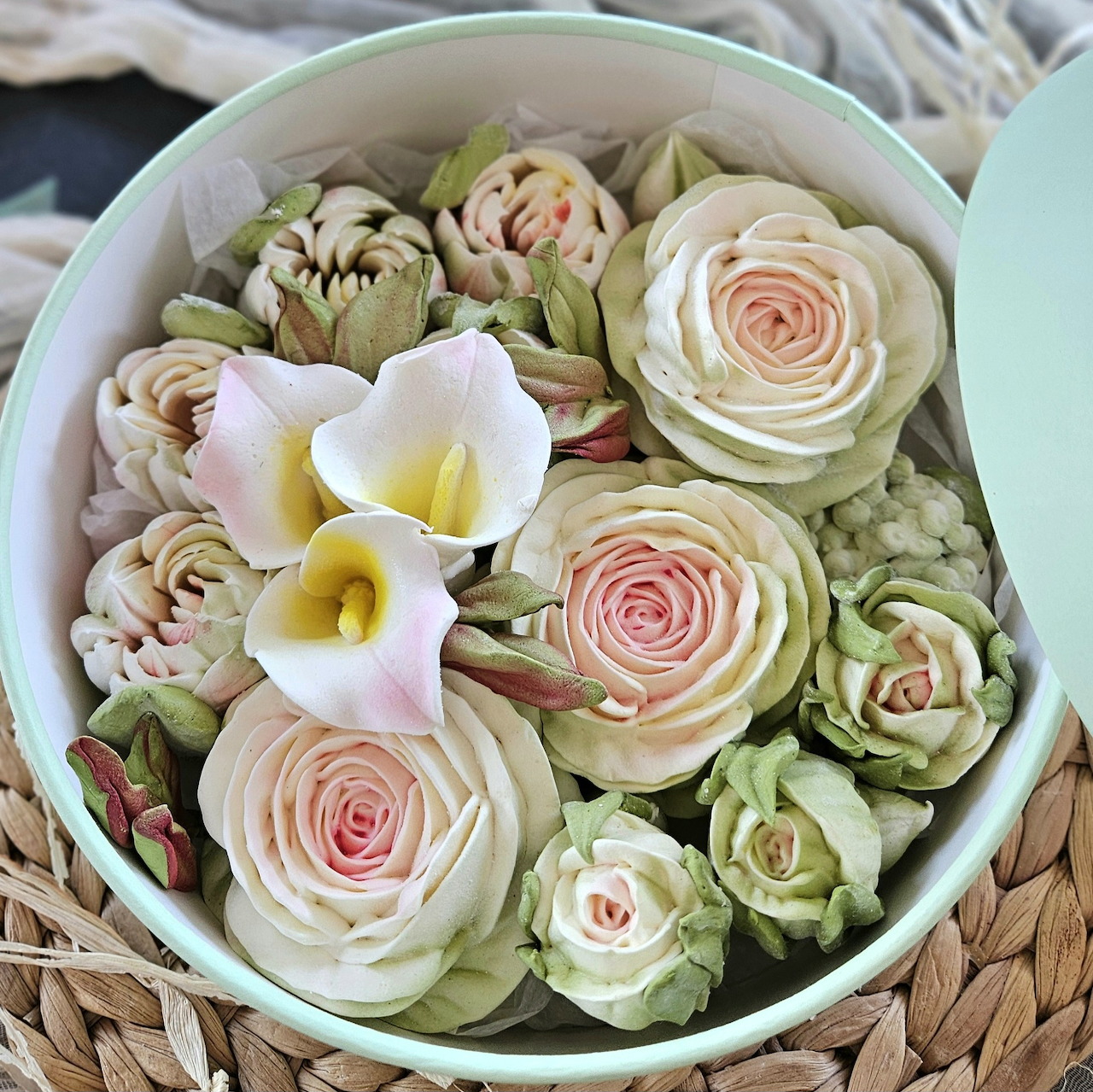 Round box of pastel flower-shaped meringues and sweets arranged like roses and lilies