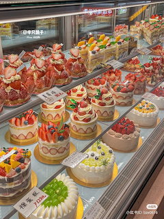 Bakery display case with assorted decorated fruit cakes and cream cakes