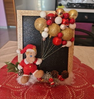 Smurf in Santa costume sitting next to a glittery frame with red, gold, and white balloon decorations