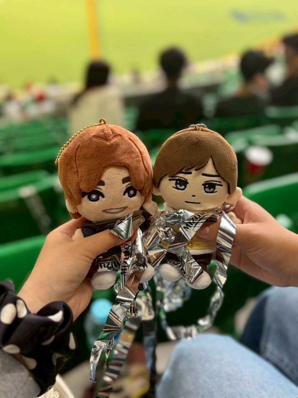 Two anime keychain figures held in hand at crowded indoor event
