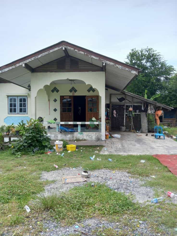 Single-story white village house with covered porch and arched window surrounded by greenery