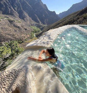 Person in infinity pool with turquoise water overlooking mountain canyon