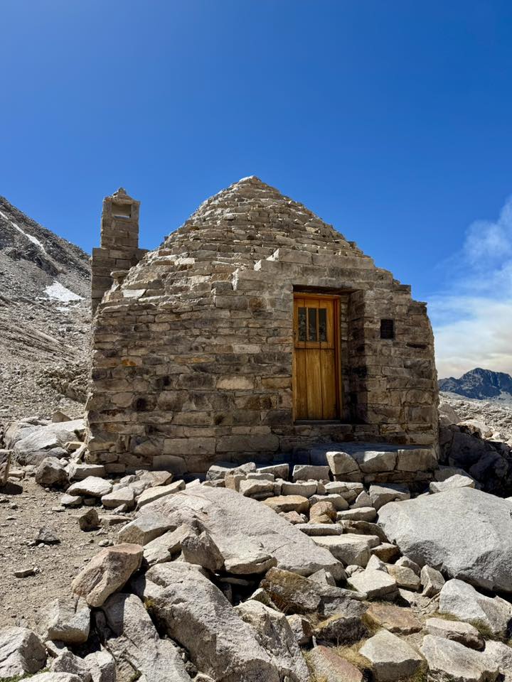 Stone mountain hut with wooden door among rocks beneath a clear blue sky