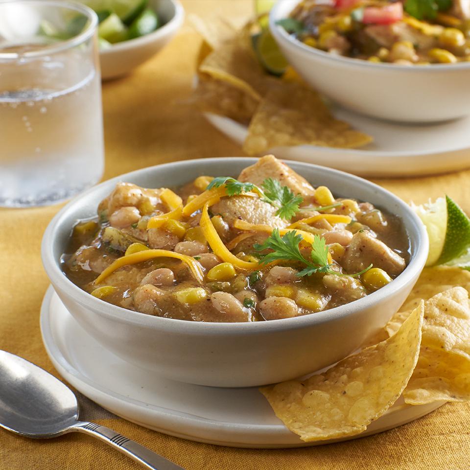 Bowl of white chicken chili with corn, beans, cheese, and cilantro, served with tortilla chips