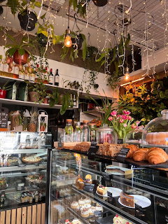 Cafe interior with pastry display cases, croissants, cakes, and hanging plants