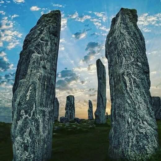 Tall ancient standing stones in a grassy field beneath a blue cloudy sky