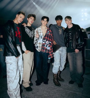 Five young men posing together indoors under stage lights
