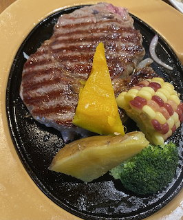 Grilled sirloin steak on a sizzling iron plate with corn, pumpkin, potato, and broccoli