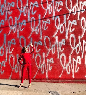 Woman in a red outfit standing before a red graffiti wall with repeated love lettering