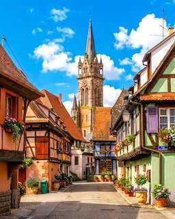 Colorful half-timbered houses on a cobblestone street in Alsace village with church steeple