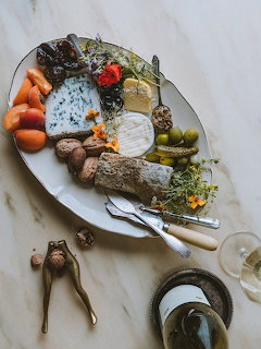 Overhead plate of French aperitif with blue cheese, bread, olives, nuts, herbs, and wine on a table