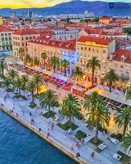 Aerial view of coastal town with palm trees, colorful buildings, and waterfront promenade at sunset