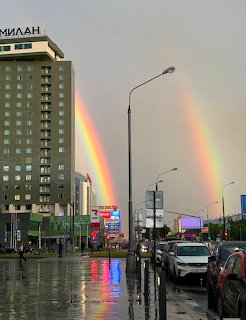 Double rainbow over rainy Moscow street with buildings and cars