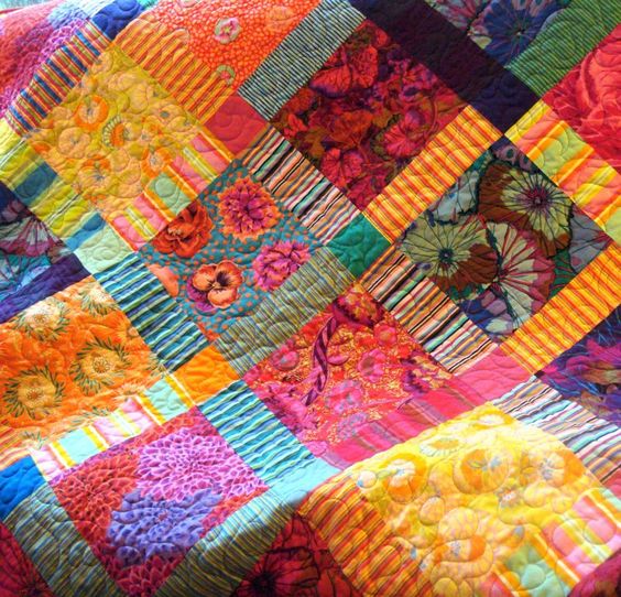 Colorful patchwork quilt with floral prints, stripes, and geometric fabric squares in bright rainbow hues
