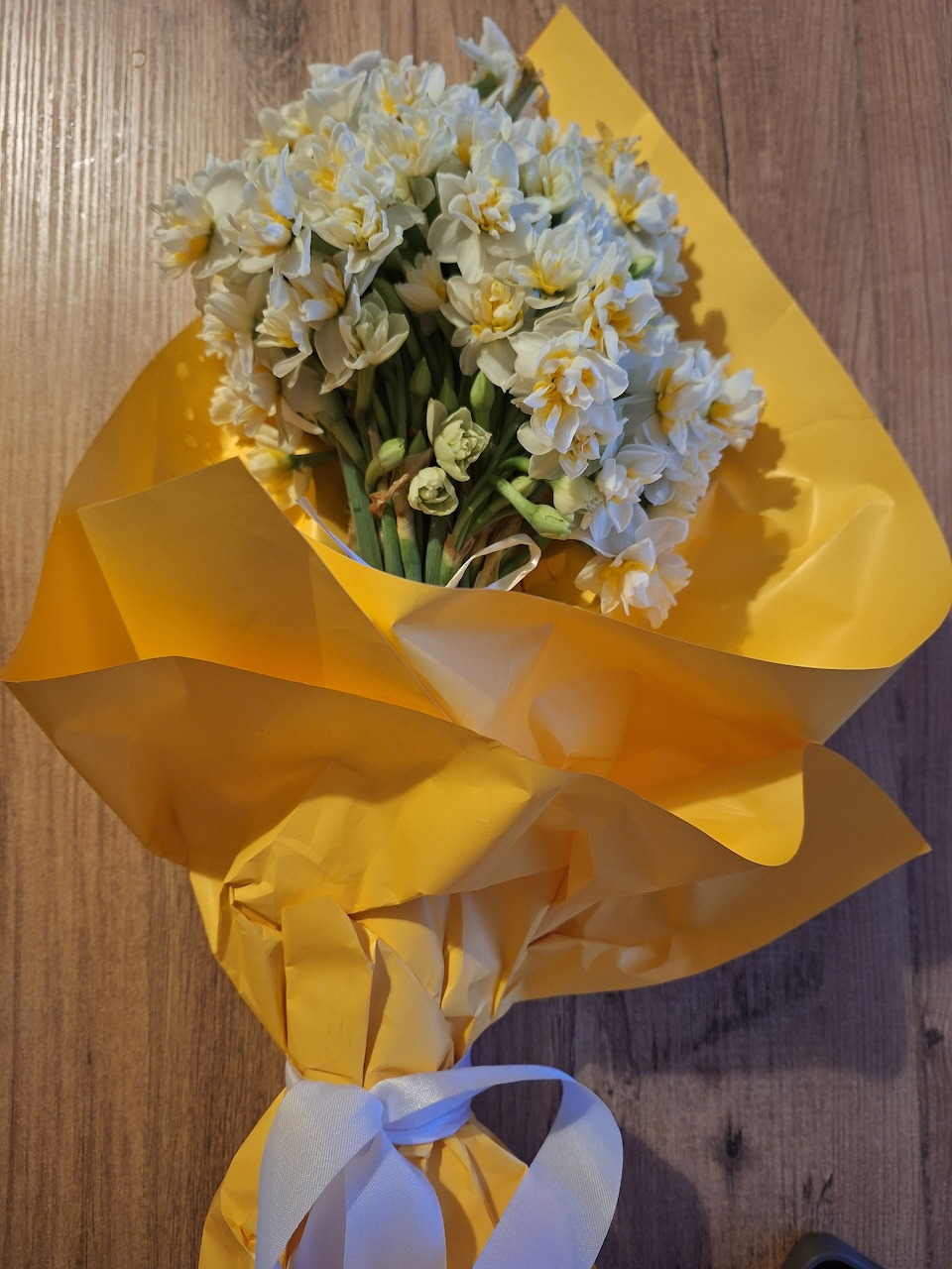White daffodil bouquet wrapped in yellow paper on wood surface