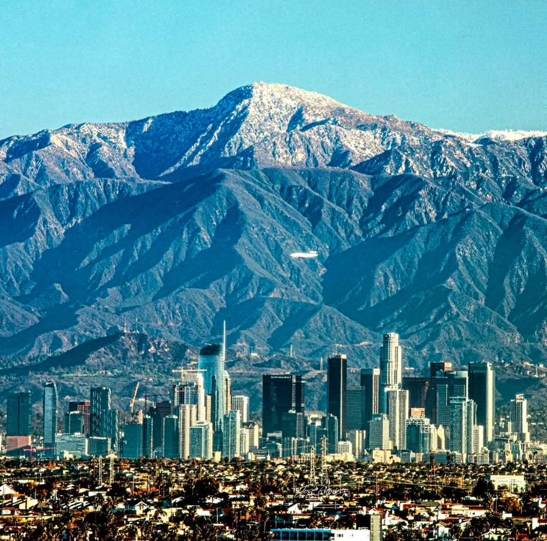 Los Angeles downtown skyline with snow-covered San Gabriel Mountains in background under blue sky