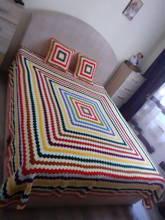 Colorful crocheted blanket with diamond pattern on a bed with matching pillows in a white room