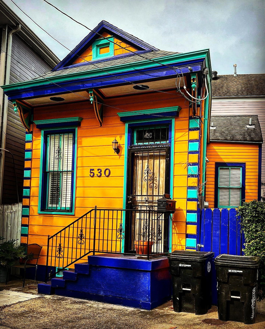 Brightly painted orange shotgun house with rainbow trim and blue porch